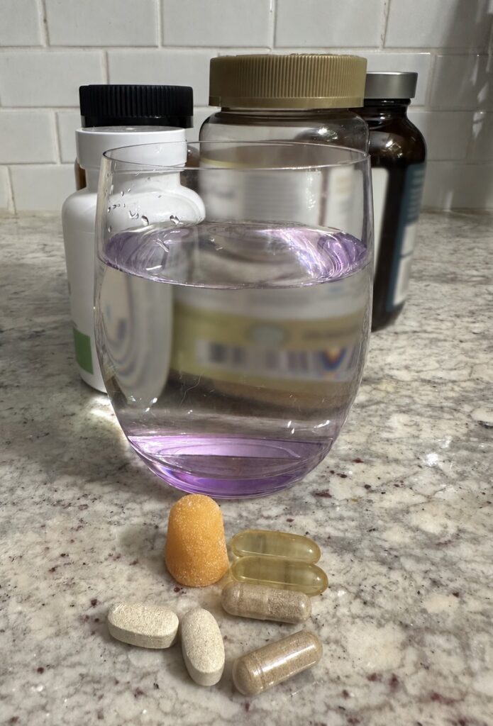 Vitamin bottles, glass of water, and vitamins sitting on a kitchen counter